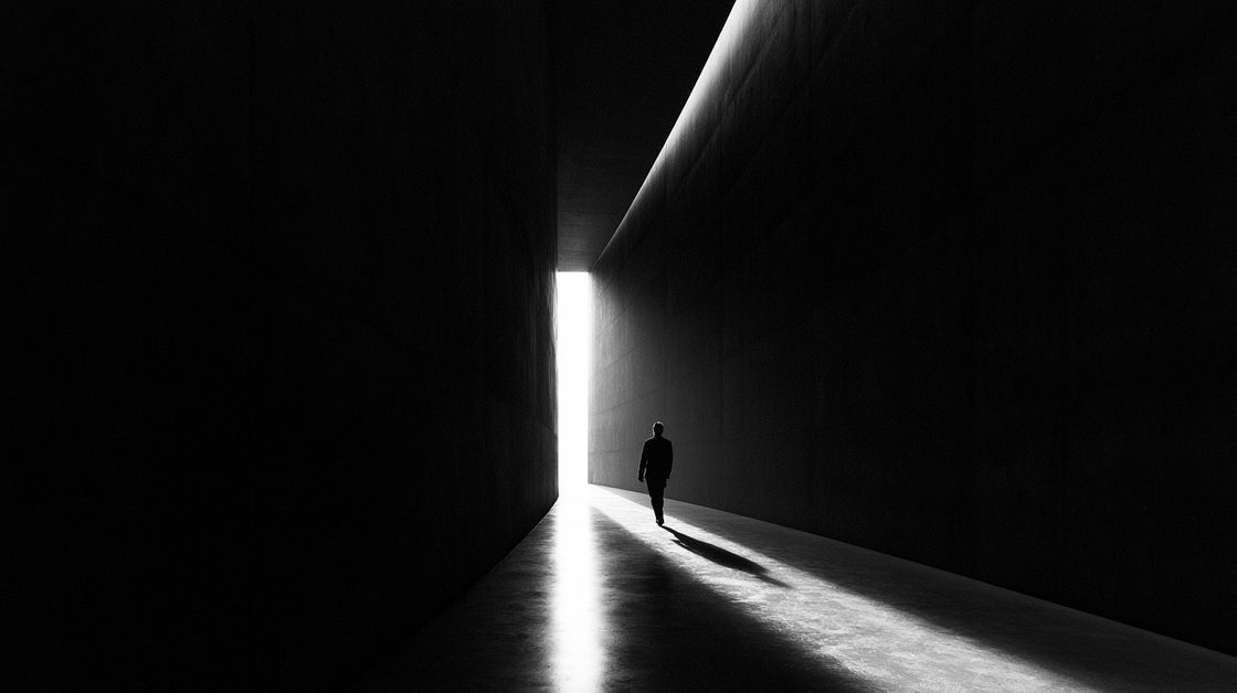 A lone figure walking a dark corridor toward an opening of light.